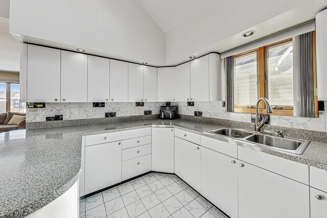 kitchen with decorative backsplash, marble finish floor, white cabinets, a sink, and vaulted ceiling
