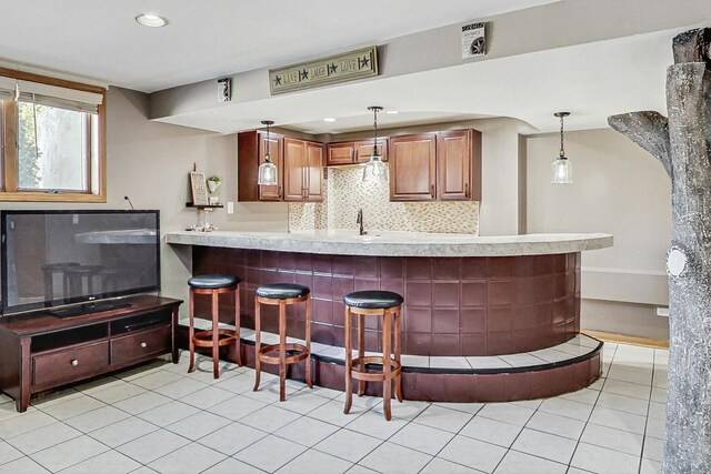 kitchen with a kitchen bar, pendant lighting, light countertops, a peninsula, and light tile patterned flooring