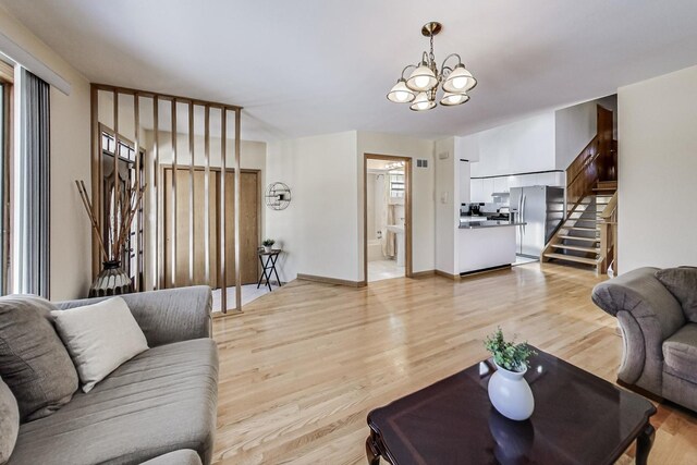 living area featuring light wood-type flooring, baseboards, a chandelier, and stairway