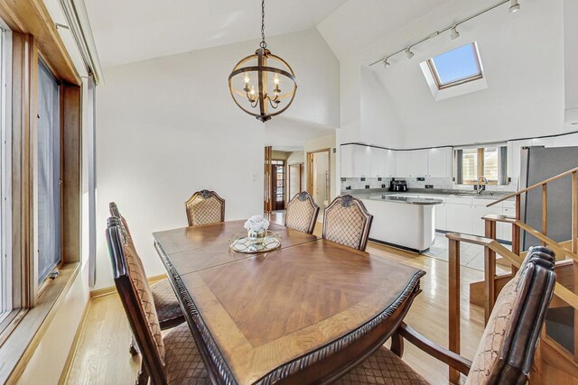 dining space with high vaulted ceiling, a chandelier, rail lighting, light wood-style flooring, and a skylight
