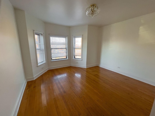 unfurnished room featuring an inviting chandelier, baseboards, and hardwood / wood-style floors