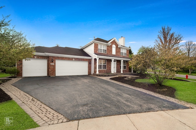 traditional home featuring covered porch, a chimney, a garage, brick siding, and aphalt driveway