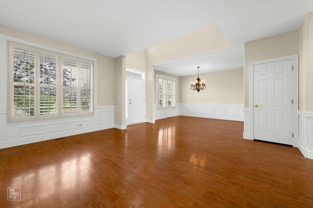 unfurnished living room featuring wainscoting, a decorative wall, wood finished floors, and a chandelier