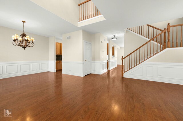 unfurnished living room featuring visible vents, wainscoting, wood finished floors, and a chandelier