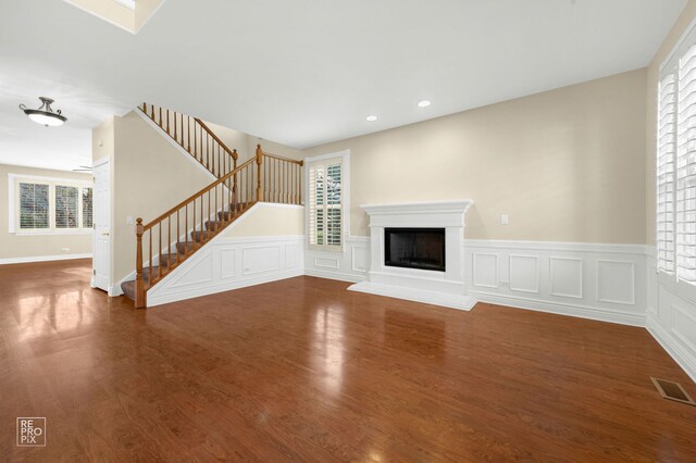 unfurnished living room with visible vents, a fireplace with raised hearth, wood finished floors, and stairway