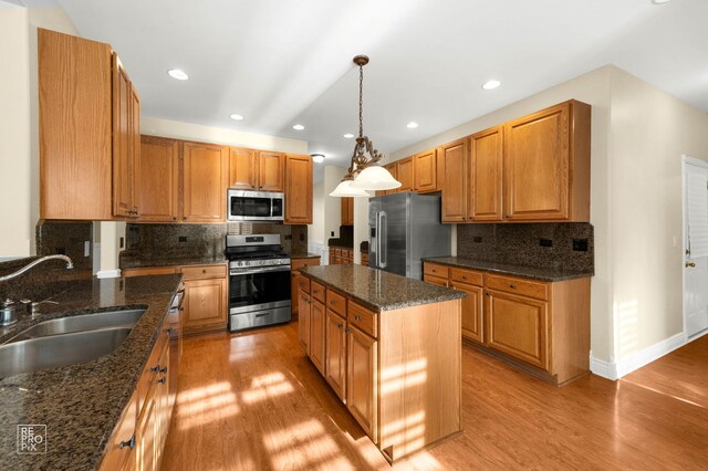 kitchen with decorative light fixtures, tasteful backsplash, a sink, light wood-style floors, and stainless steel appliances