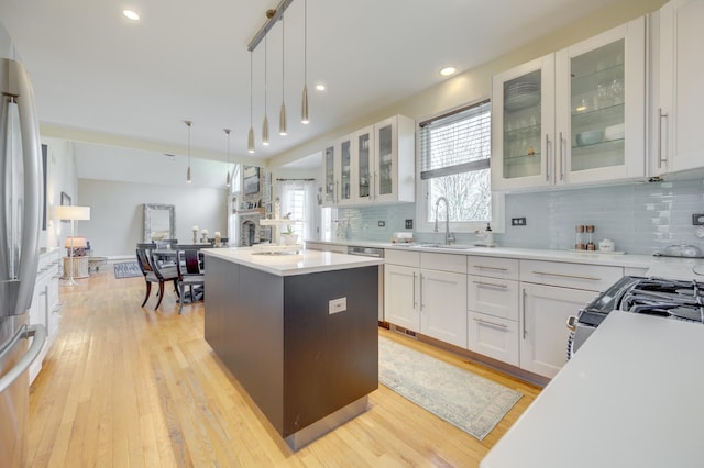kitchen featuring white cabinets, a sink, light countertops, a center island, and decorative backsplash