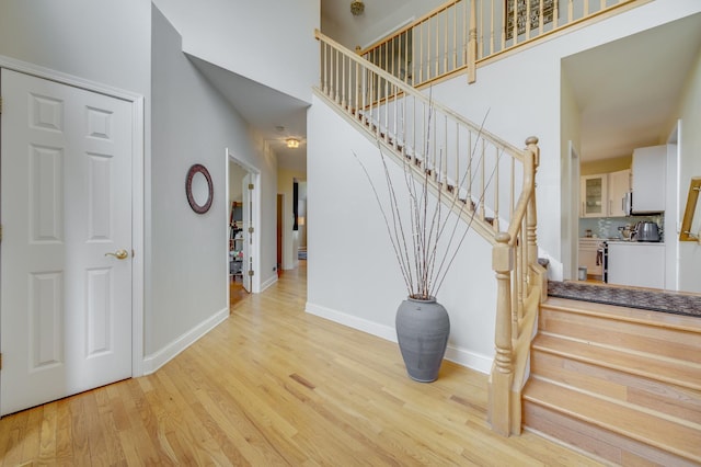staircase featuring baseboards, wood finished floors, and a high ceiling