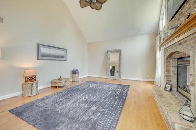 unfurnished living room with ceiling fan, a brick fireplace, high vaulted ceiling, baseboards, and wood finished floors