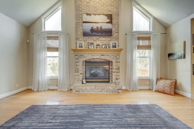 unfurnished living room with a healthy amount of sunlight, high vaulted ceiling, a brick fireplace, and wood finished floors