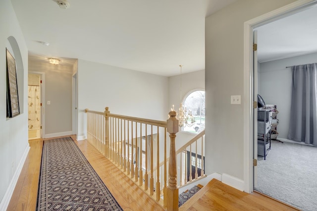 hallway featuring a chandelier, baseboards, an upstairs landing, and wood finished floors