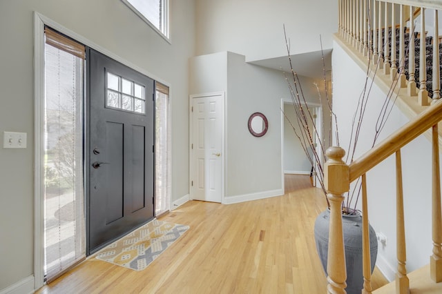 foyer entrance with stairs, baseboards, a wealth of natural light, wood finished floors, and a towering ceiling