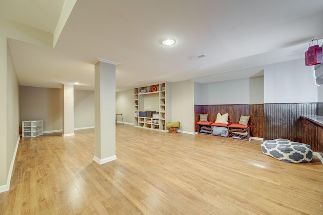 finished below grade area featuring visible vents, baseboards, light wood-type flooring, a wainscoted wall, and built in shelves