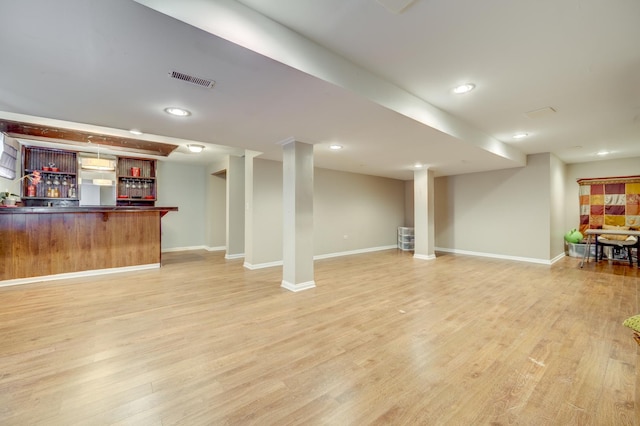 finished basement with a bar, light wood finished floors, baseboards, and visible vents