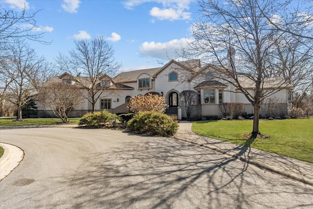 french country inspired facade featuring aphalt driveway, a front lawn, and stucco siding