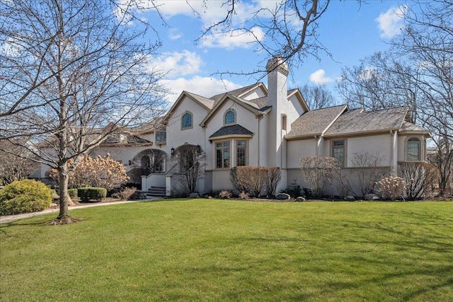 view of front facade with a front lawn, roof with shingles, stucco siding, and a chimney