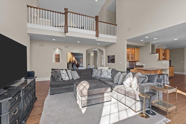 living room with arched walkways, baseboards, wood finished floors, and a towering ceiling