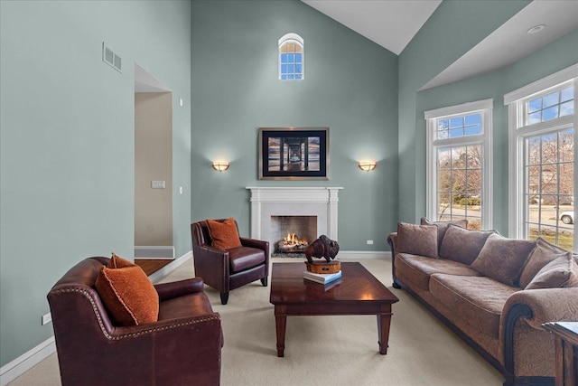 carpeted living room featuring baseboards, a warm lit fireplace, high vaulted ceiling, and visible vents