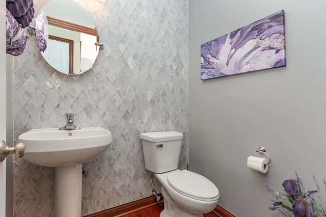 half bath with baseboards, toilet, and wood finished floors