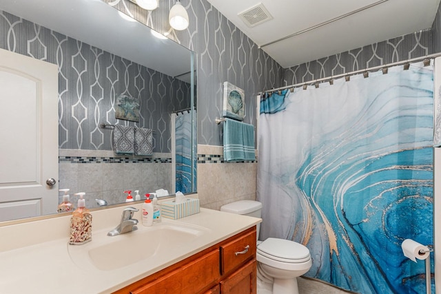 bathroom with vanity, visible vents, toilet, tile walls, and wallpapered walls