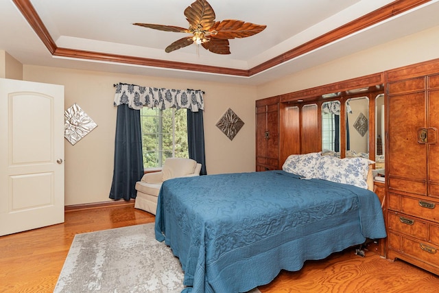 bedroom with baseboards, a ceiling fan, a tray ceiling, and wood finished floors