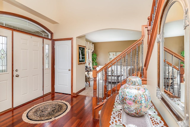entryway with baseboards, arched walkways, stairs, and wood finished floors