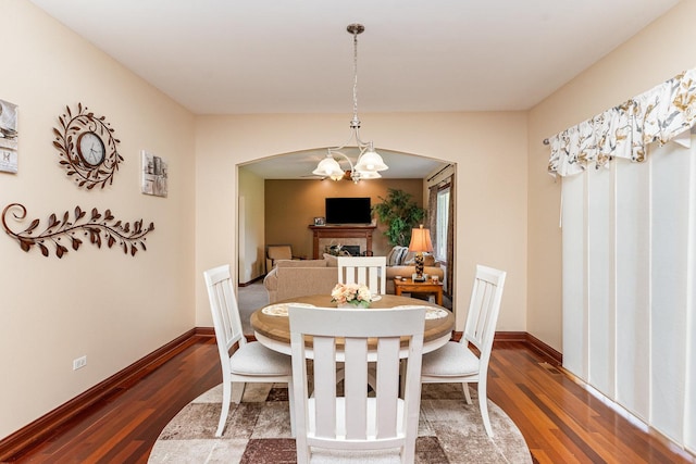 dining room with an inviting chandelier, wood finished floors, a fireplace, baseboards, and arched walkways