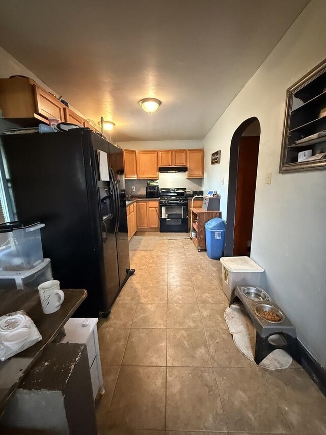 1004 Nowell Ave, Joliet, IL 60433 - kitchen with dark countertops, arched walkways, light tile patterned floors, under cabinet range hood, and black appliances