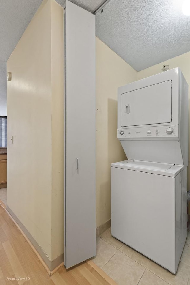 laundry area featuring laundry area, stacked washer and dryer, baseboards, and light wood finished floors