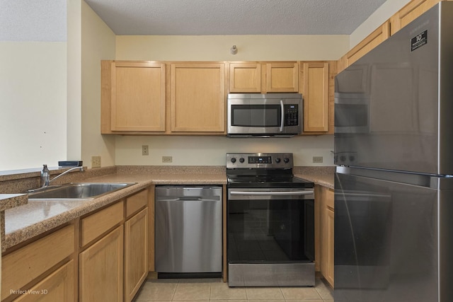 kitchen featuring light brown cabinetry, a textured ceiling, a sink, appliances with stainless steel finishes, and light tile patterned floors