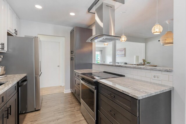kitchen featuring light stone countertops, island range hood, light wood-type flooring, hanging light fixtures, and stainless steel appliances
