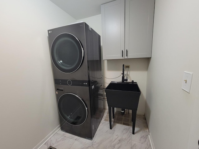 laundry room featuring baseboards, stacked washer and clothes dryer, cabinet space, and marble finish floor