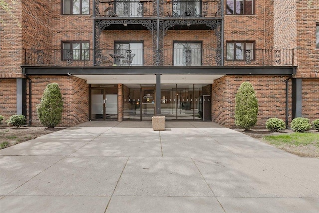 property entrance with brick siding, driveway, and a balcony