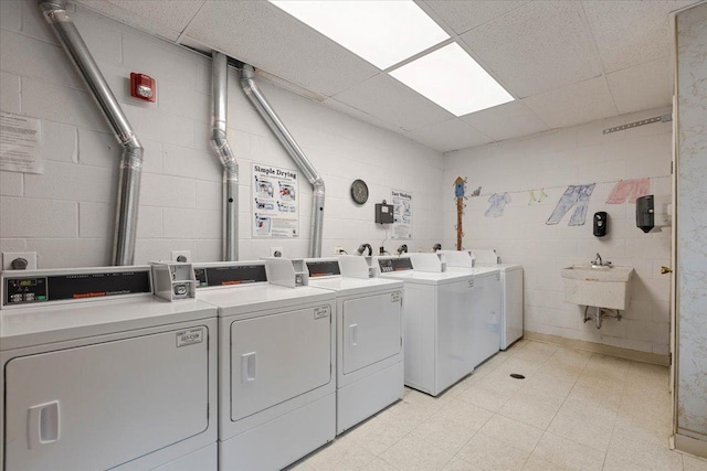 community laundry room with washer and clothes dryer, light floors, a sink, and concrete block wall