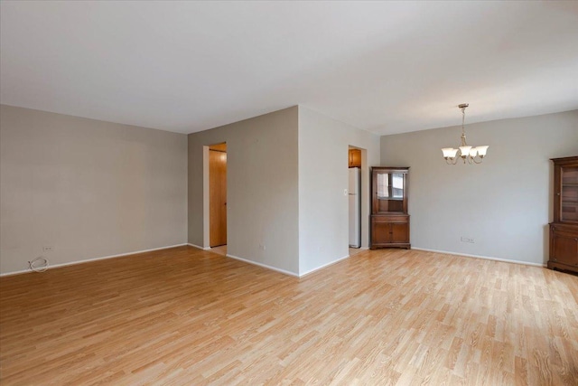 empty room with a chandelier, baseboards, and light wood finished floors