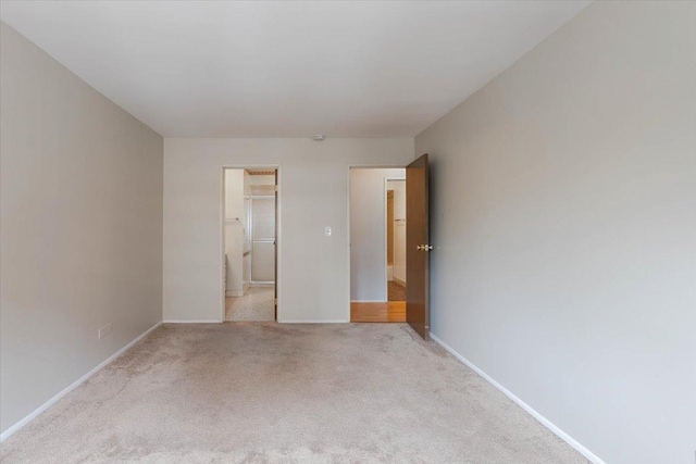 unfurnished bedroom featuring baseboards, light colored carpet, and a walk in closet