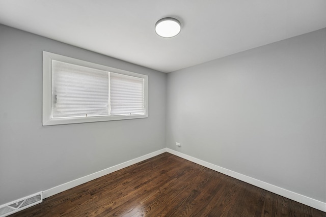 spare room featuring baseboards, dark wood-style floors, and visible vents