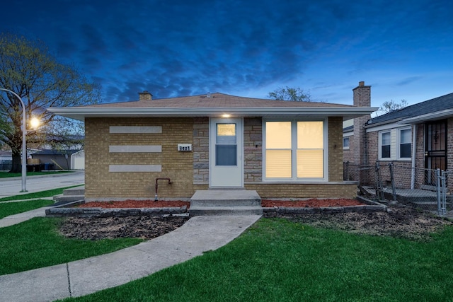 bungalow featuring a chimney, a yard, brick siding, and fence