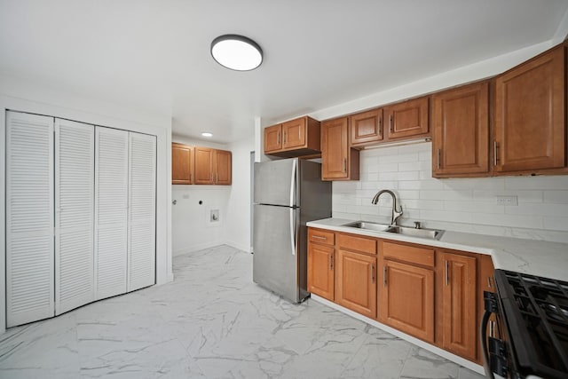 kitchen with a sink, marble finish floor, brown cabinets, freestanding refrigerator, and gas stove