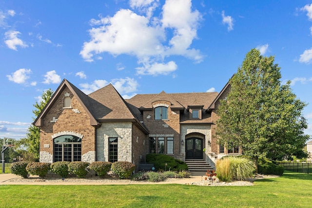 french provincial home with fence, stone siding, brick siding, a front yard, and french doors