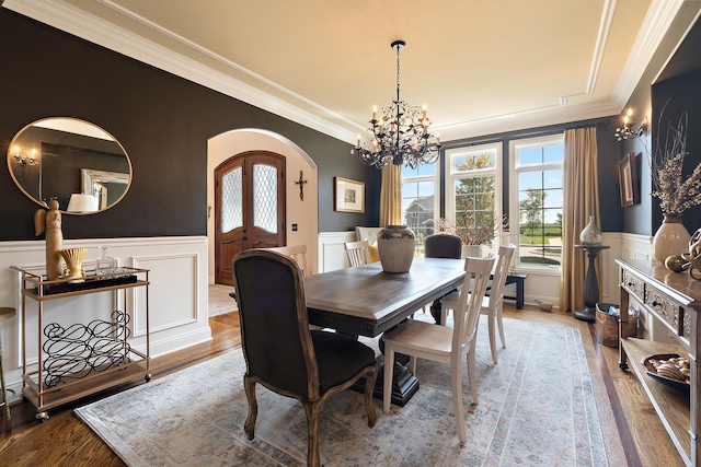 dining room featuring arched walkways, ornamental molding, a decorative wall, and a chandelier