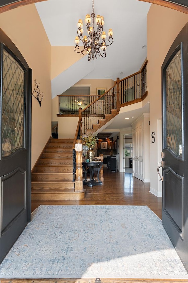 entrance foyer featuring an inviting chandelier, stairs, baseboards, wood finished floors, and a towering ceiling