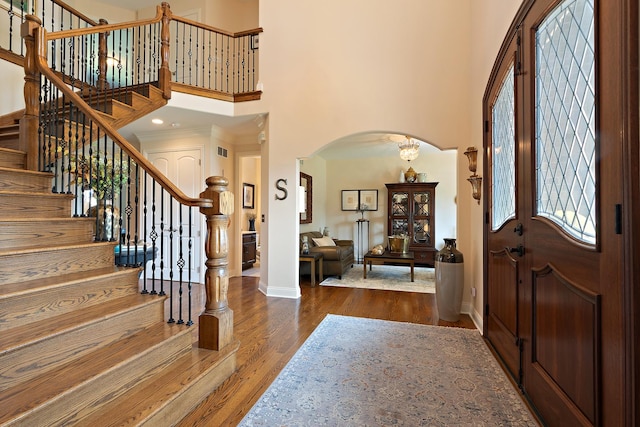 entryway with arched walkways, wood finished floors, baseboards, a high ceiling, and stairs