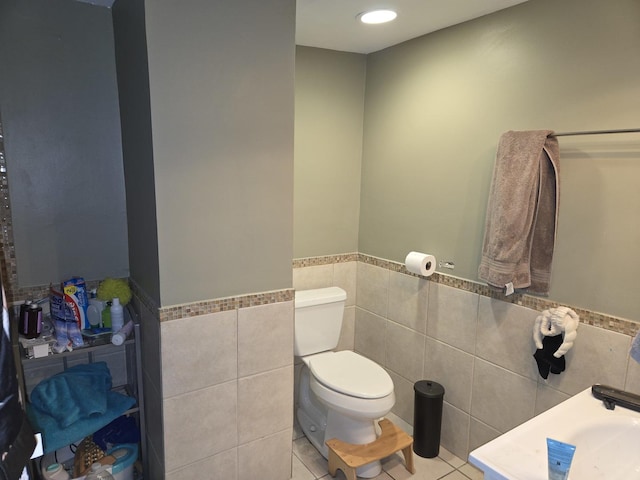 bathroom with toilet, tile patterned floors, tile walls, and wainscoting
