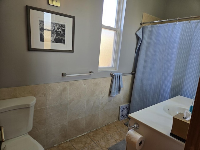 bathroom featuring toilet, tile patterned floors, tile walls, and wainscoting