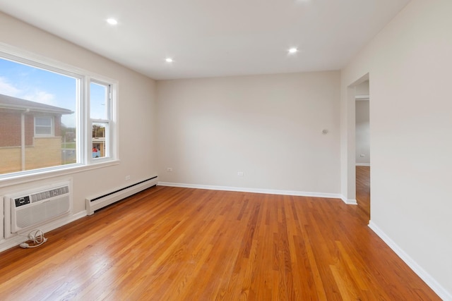 spare room featuring baseboards, a baseboard radiator, an AC wall unit, and light wood finished floors