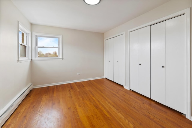 unfurnished bedroom with multiple closets, a baseboard radiator, baseboards, and light wood finished floors
