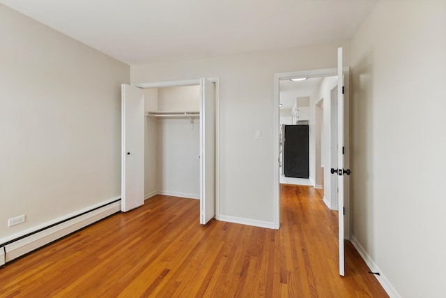 unfurnished bedroom featuring baseboards, baseboard heating, a closet, and light wood finished floors