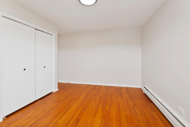unfurnished bedroom with a closet, light wood-style floors, baseboards, and a baseboard radiator