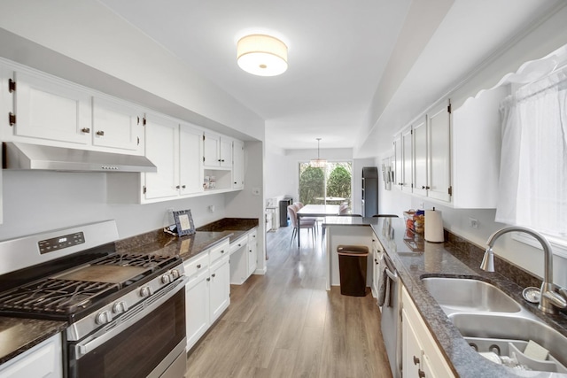 kitchen with stainless steel gas stove, light wood-style floors, white cabinetry, under cabinet range hood, and a sink